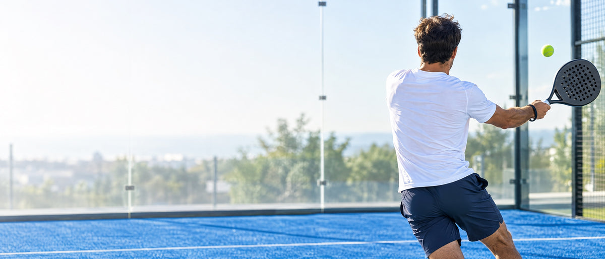 Padel player hitting a backhand on a blue padel court with glass walls